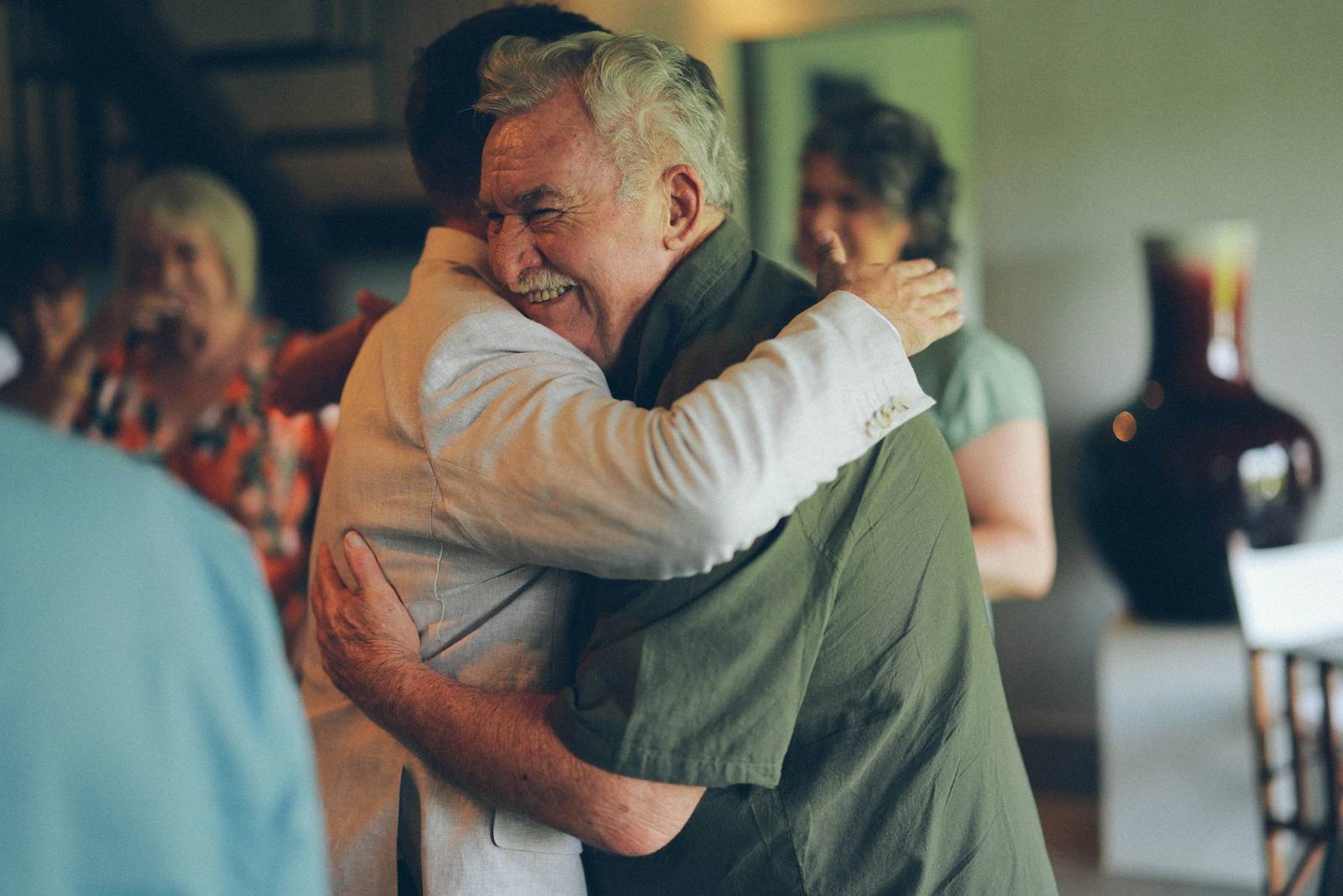 Senior man embracing another adult while family members look on