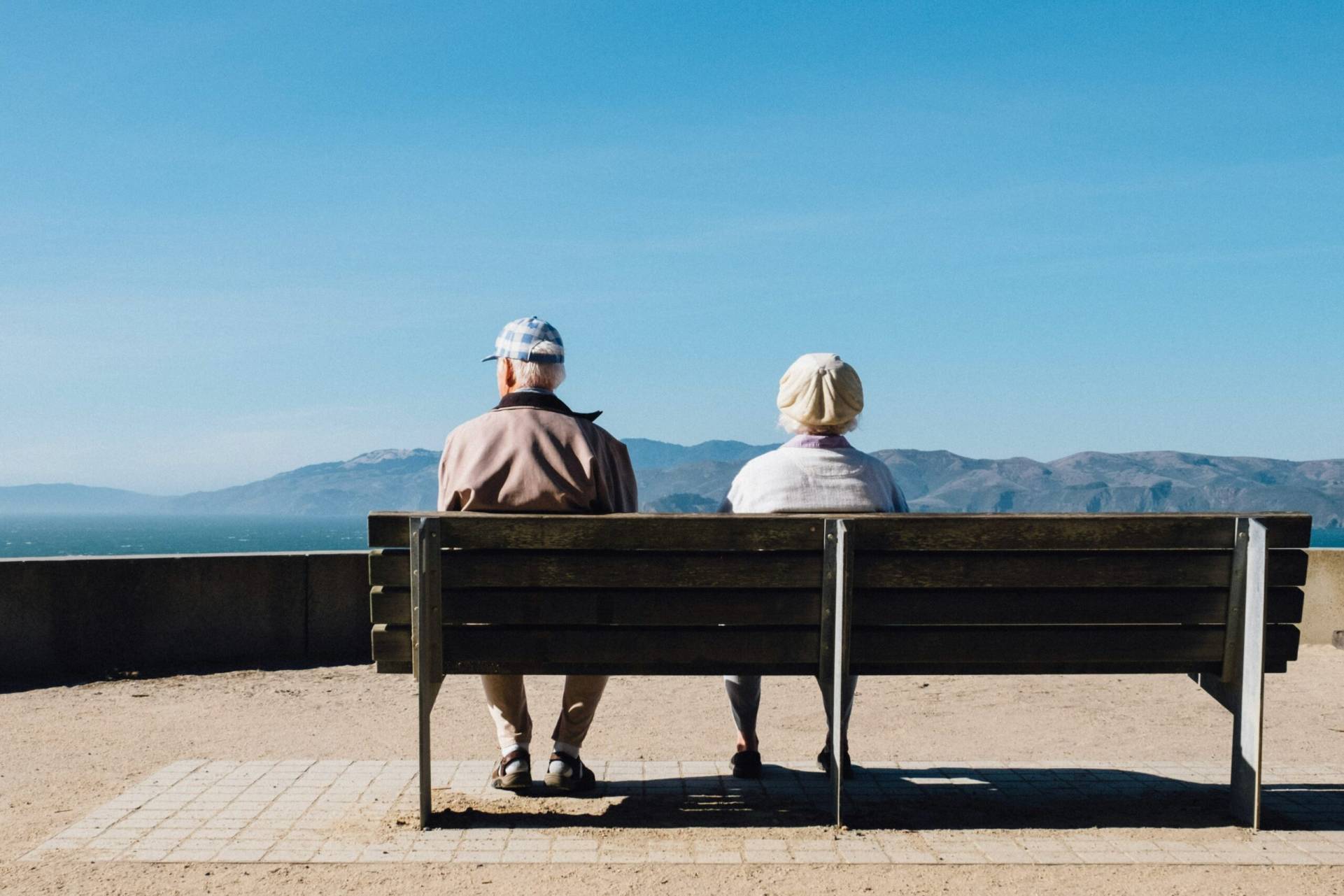Elderly couple sitting on a bench facing the ocean and mountains