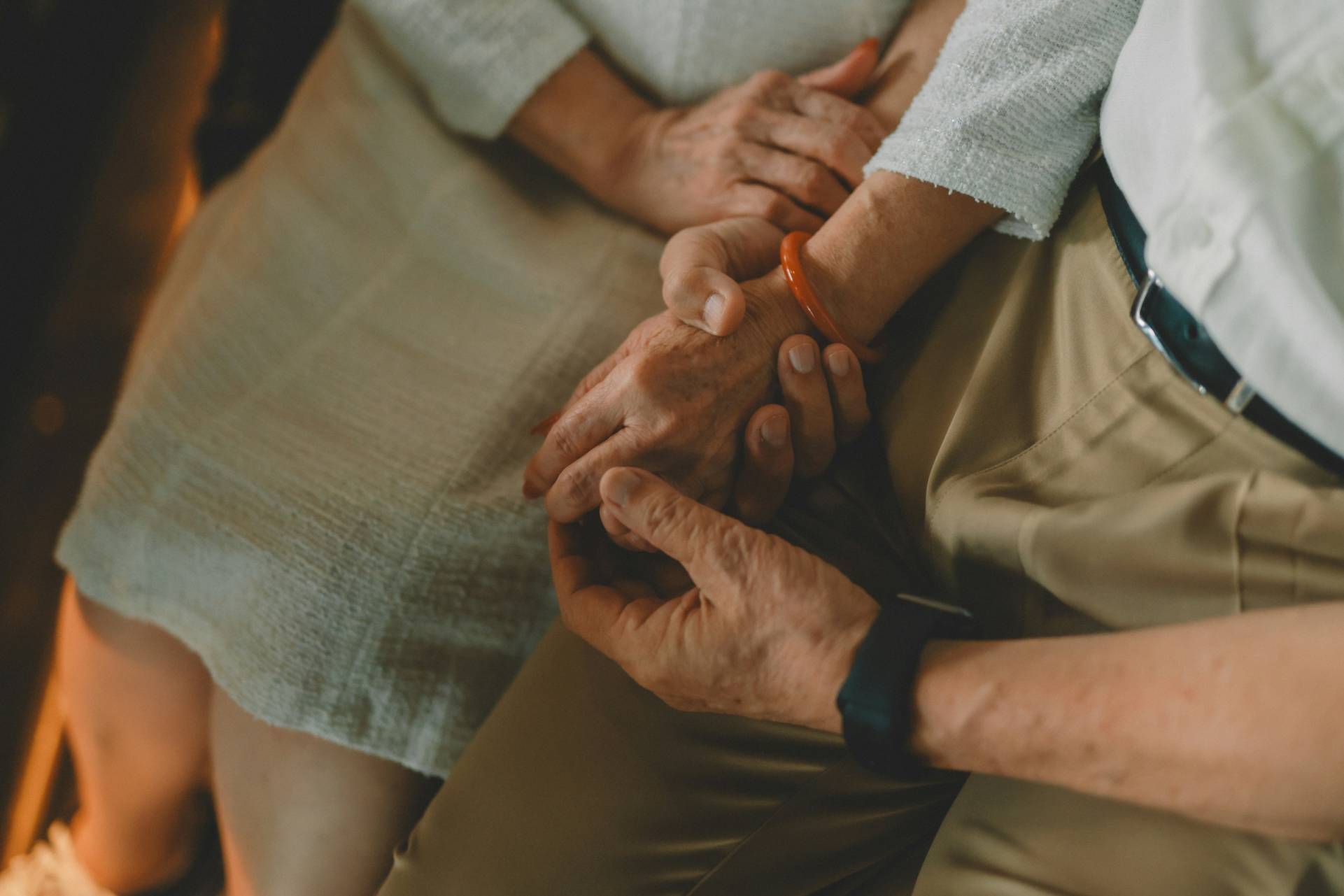 Close-up of an adult holding an elderly person’s hands while seated together